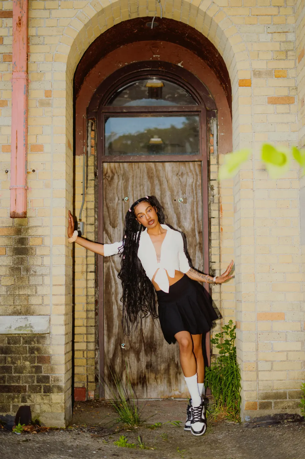 Woman leaning in the arched, boarded doorway of an abandoned school