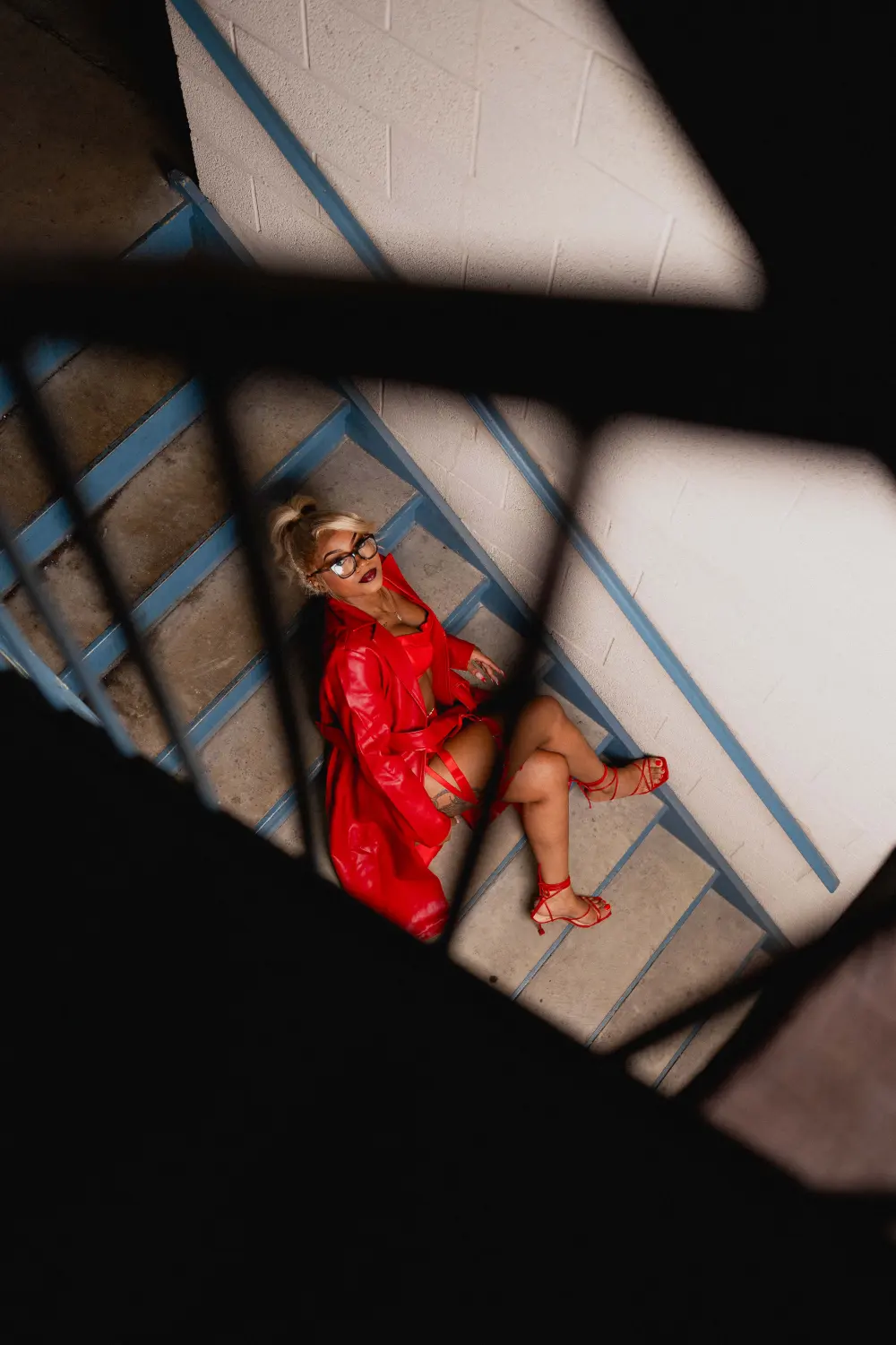 Woman in a red leather coat lying on a stairwell landing, shot from above through the railings