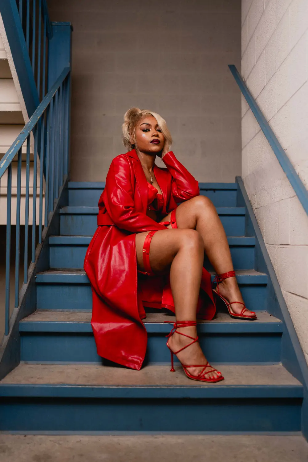 Woman in glasses and a red leather coat seated on blue stairwell steps