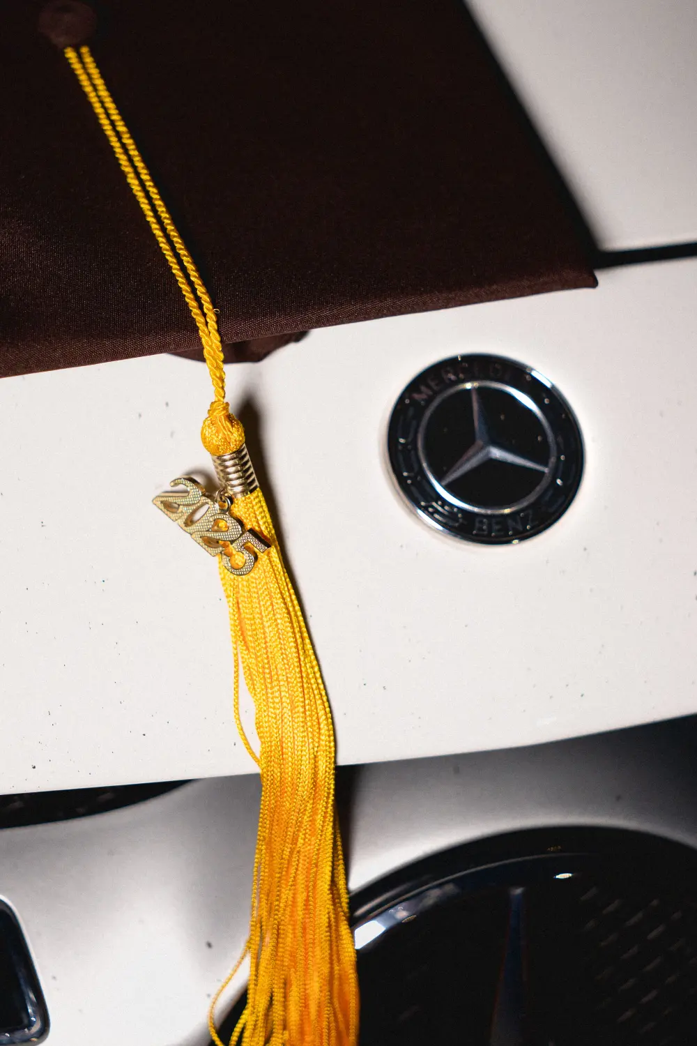 Graduation cap with a gold tassel and 2025 charm resting on the hood of a white car