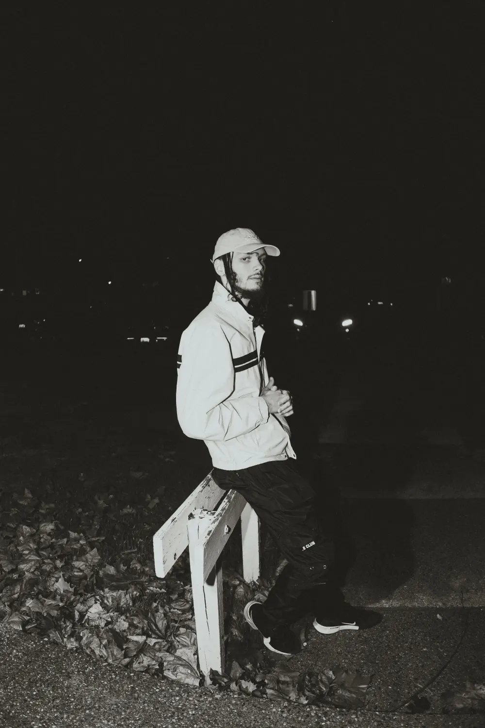 Joey in a cap and white jacket sitting on a wooden post, black and white