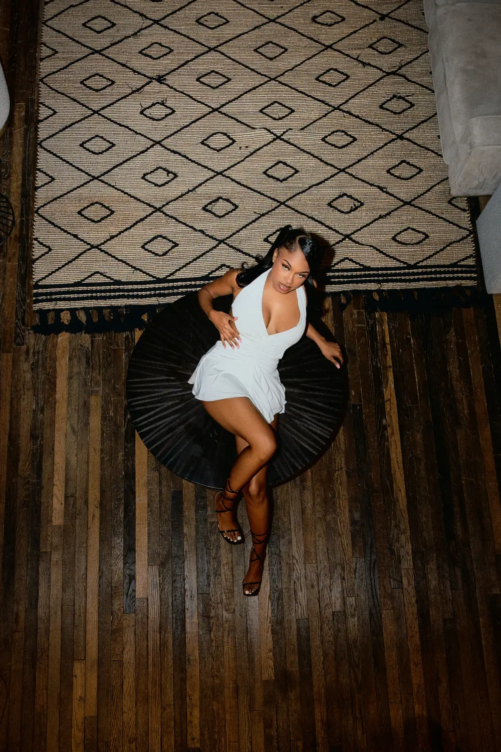 Woman in a white dress on a black disc chair, shot from above on a patterned rug