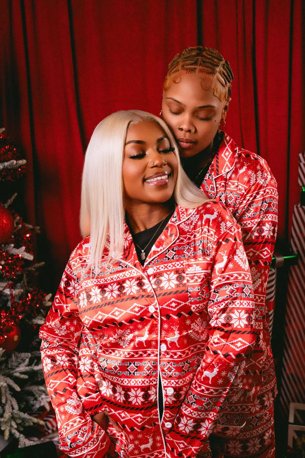 Couple in matching red holiday pajamas embracing in front of a Christmas tree