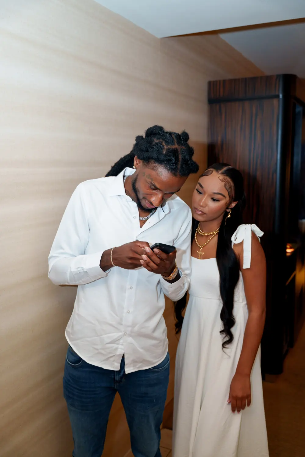 Couple in white looking at a phone together in a hotel hallway