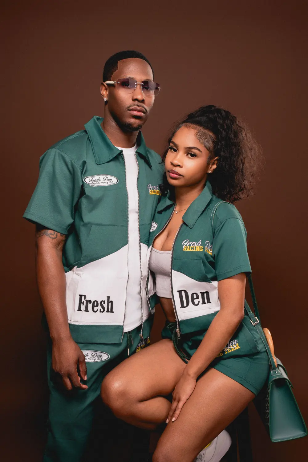 Couple in matching green work shirts posing close together against a brown studio backdrop