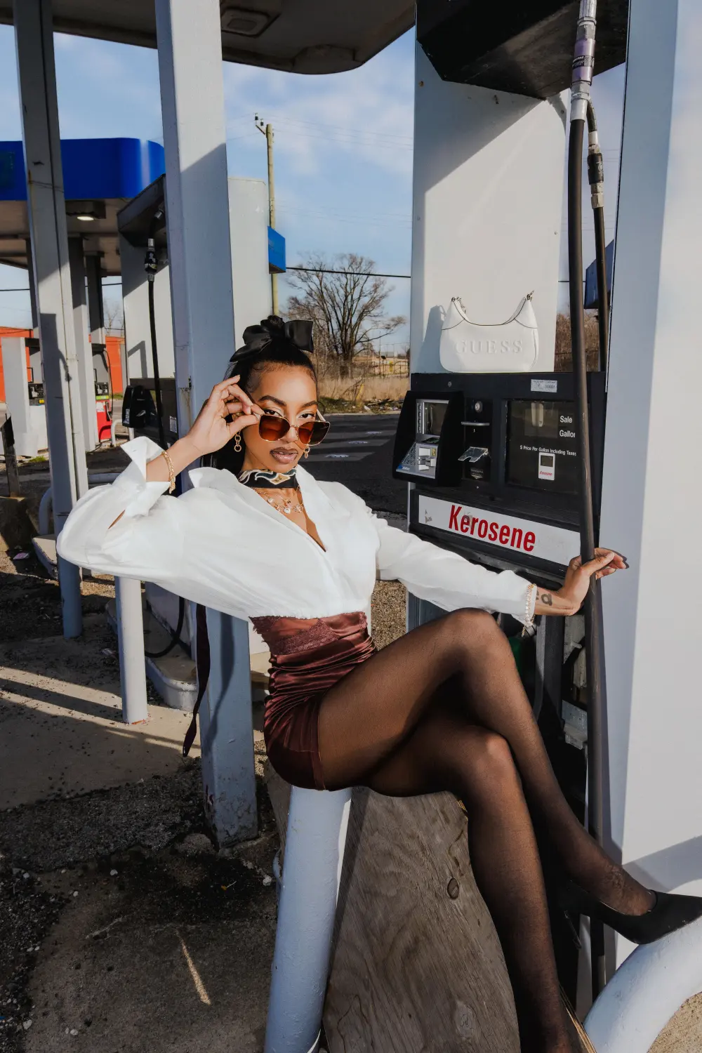 Woman in sunglasses and a white blouse sitting on a gas pump barrier
