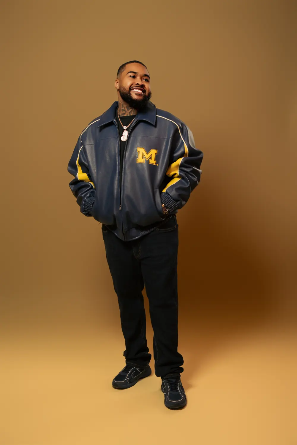 Man in a navy and gold varsity jacket standing against a tan backdrop