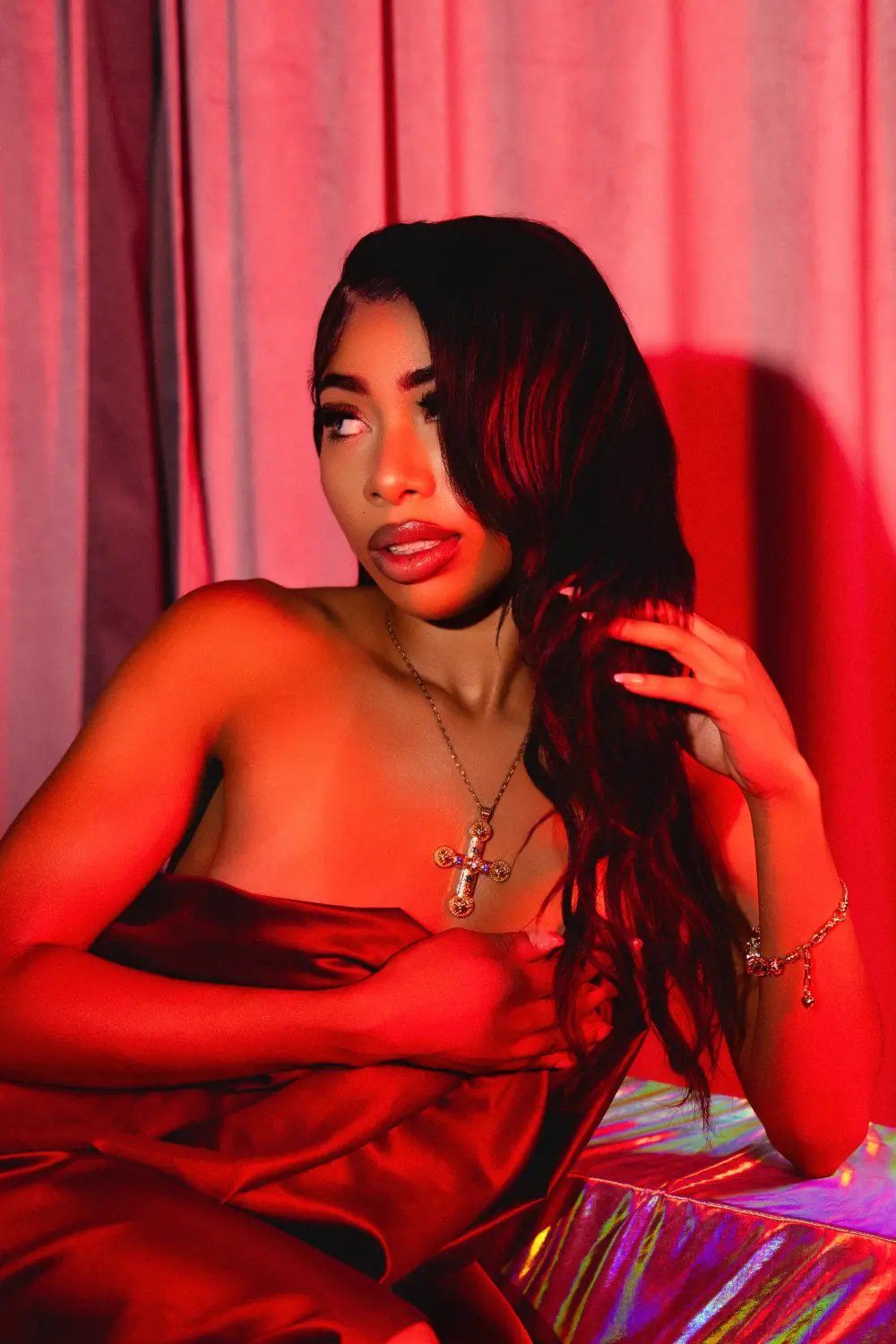 Close portrait of a woman in red satin, hand in her hair, in red light by a curtain