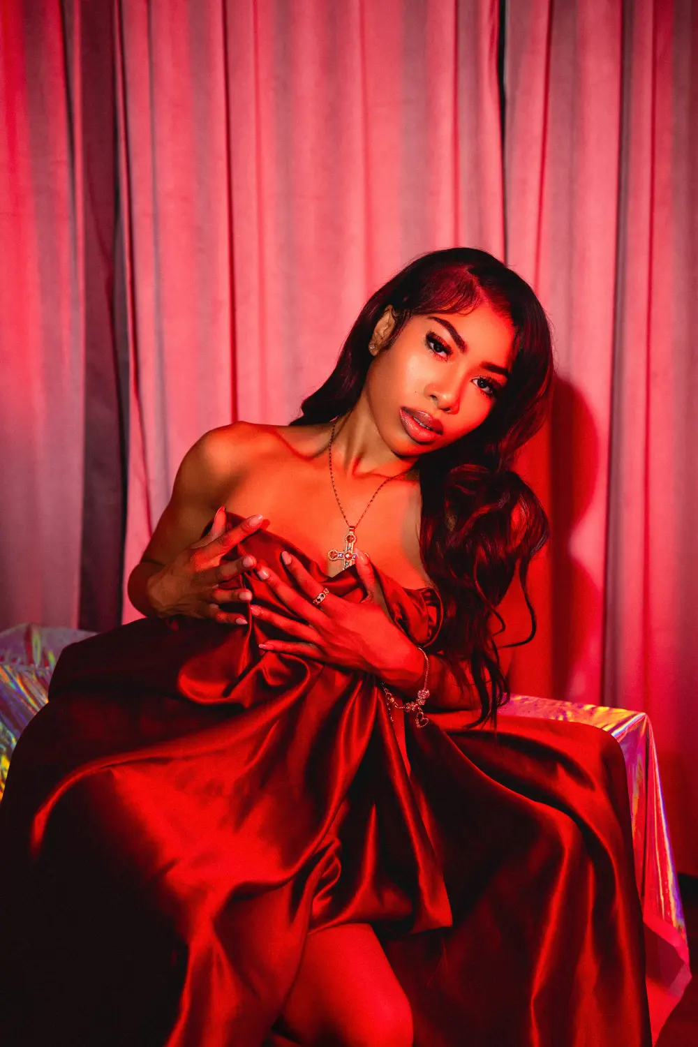 Woman in red satin holding the fabric at her chest, red curtains behind her