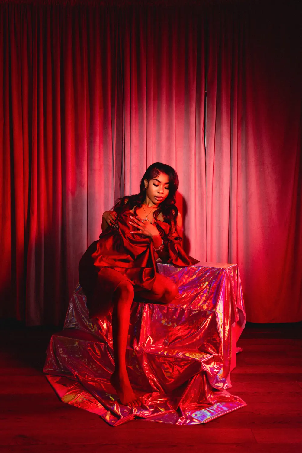 Woman draped in red satin seated in front of red stage curtains