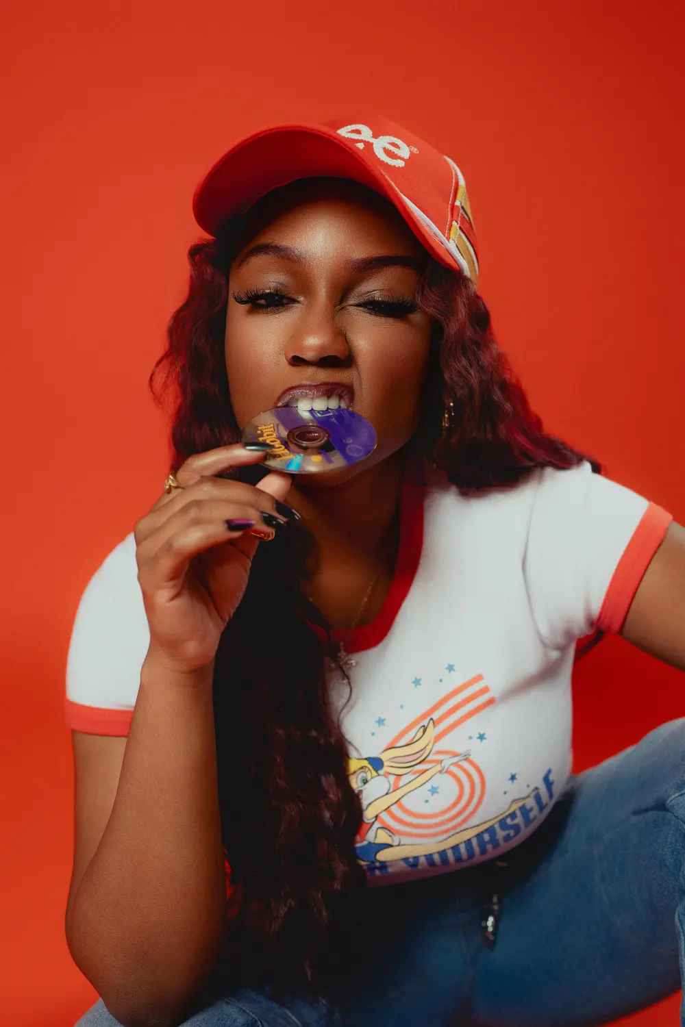 Woman in a red cap biting a ring pop against a red backdrop