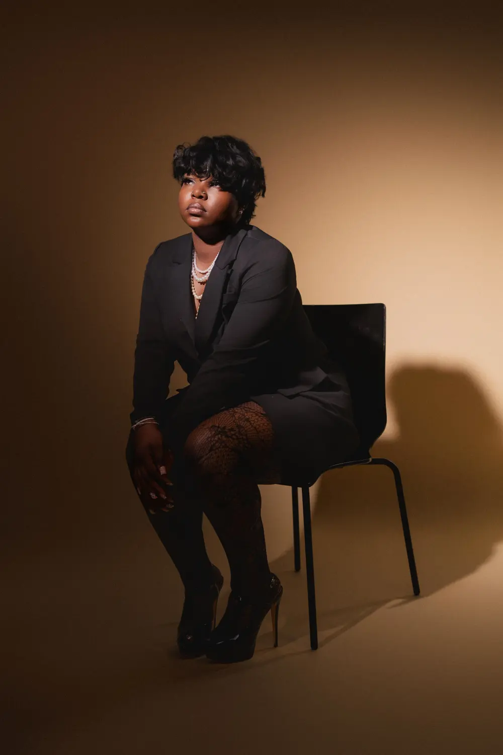 Woman in a dark suit seated on a chair in warm studio light
