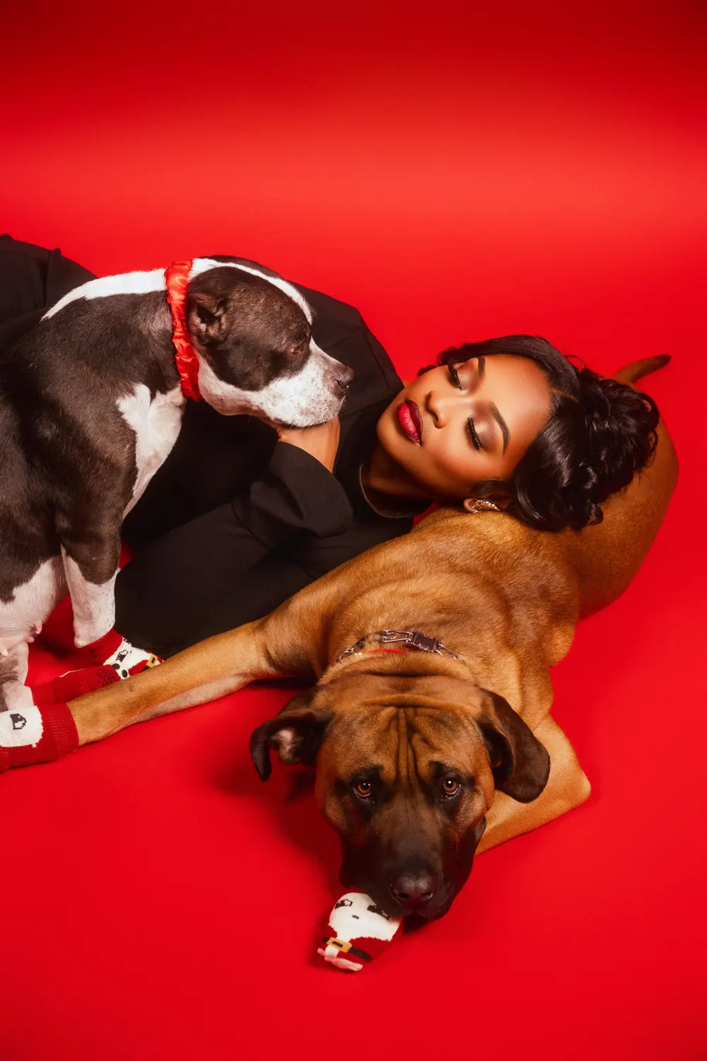 Woman lying on a red backdrop with her two dogs